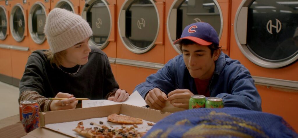 two young men eat pizza in a laundry place in the film dirty laundry